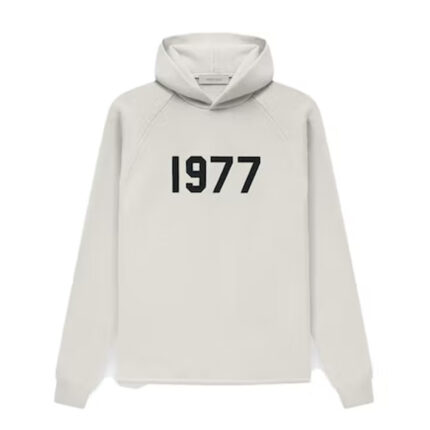 "Fear of God Essentials 1977 Knit Hoodie in Wheat: Elevate your casual wardrobe with this vintage-inspired knit hoodie from Fear of God Essentials. The warm wheat color adds a touch of nostalgia to the classic design. Embrace both comfort and style effortlessly with this essential piece that complements your urban lifestyle."